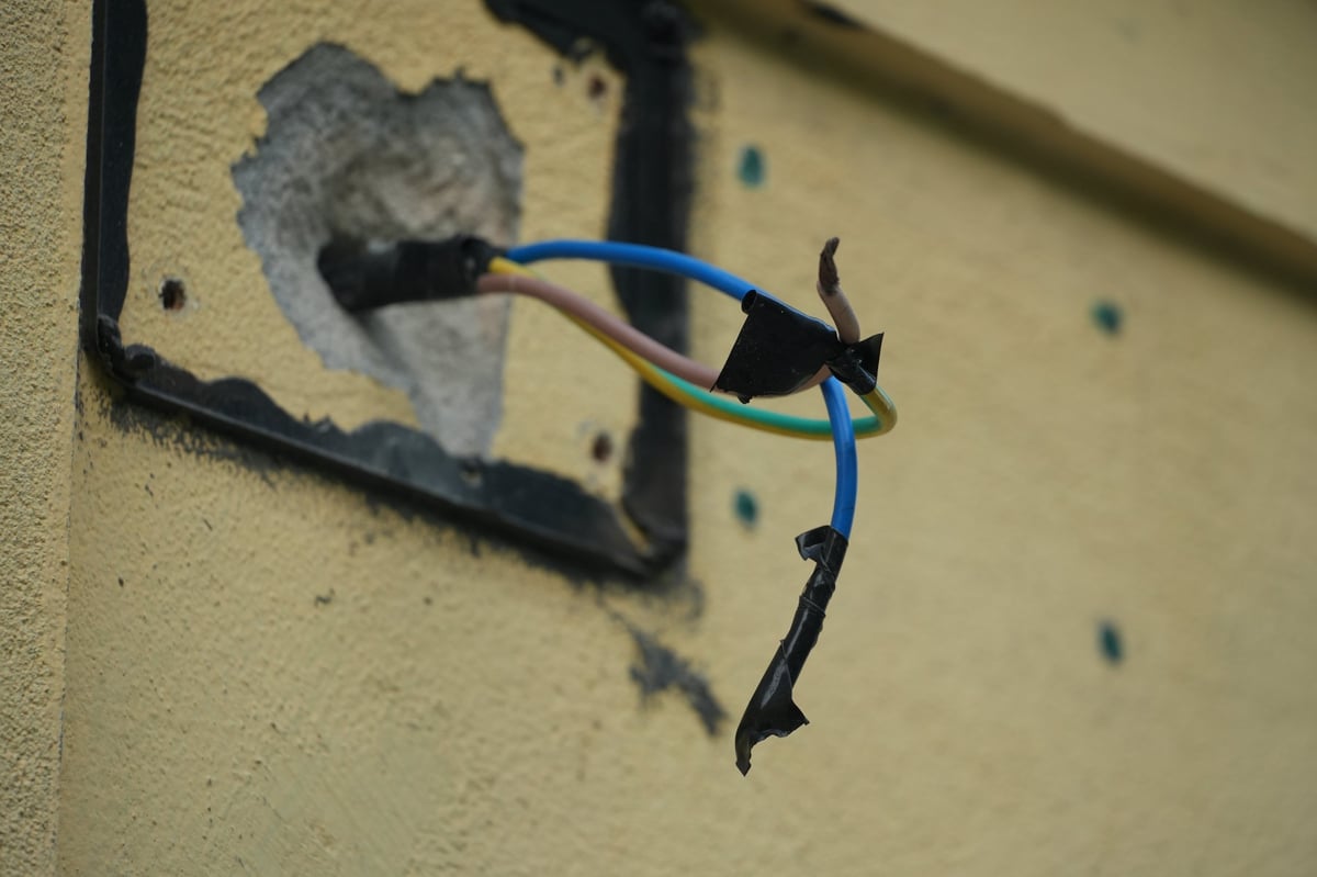 Damaged electrical wires protruding from a wall socket, indicating a potential safety hazard