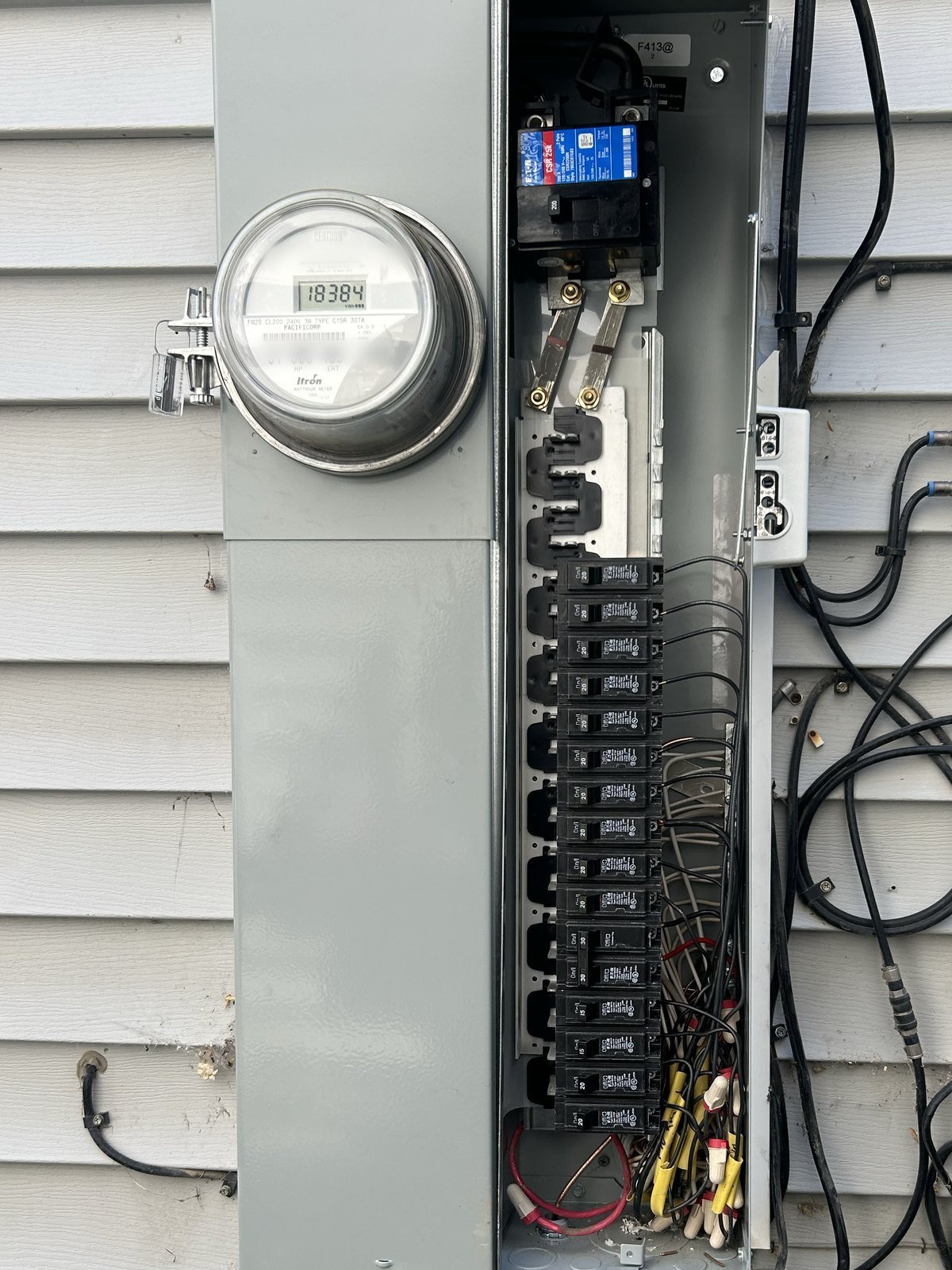 Electric meter and circuit breaker panel mounted on white siding with visible wiring connections