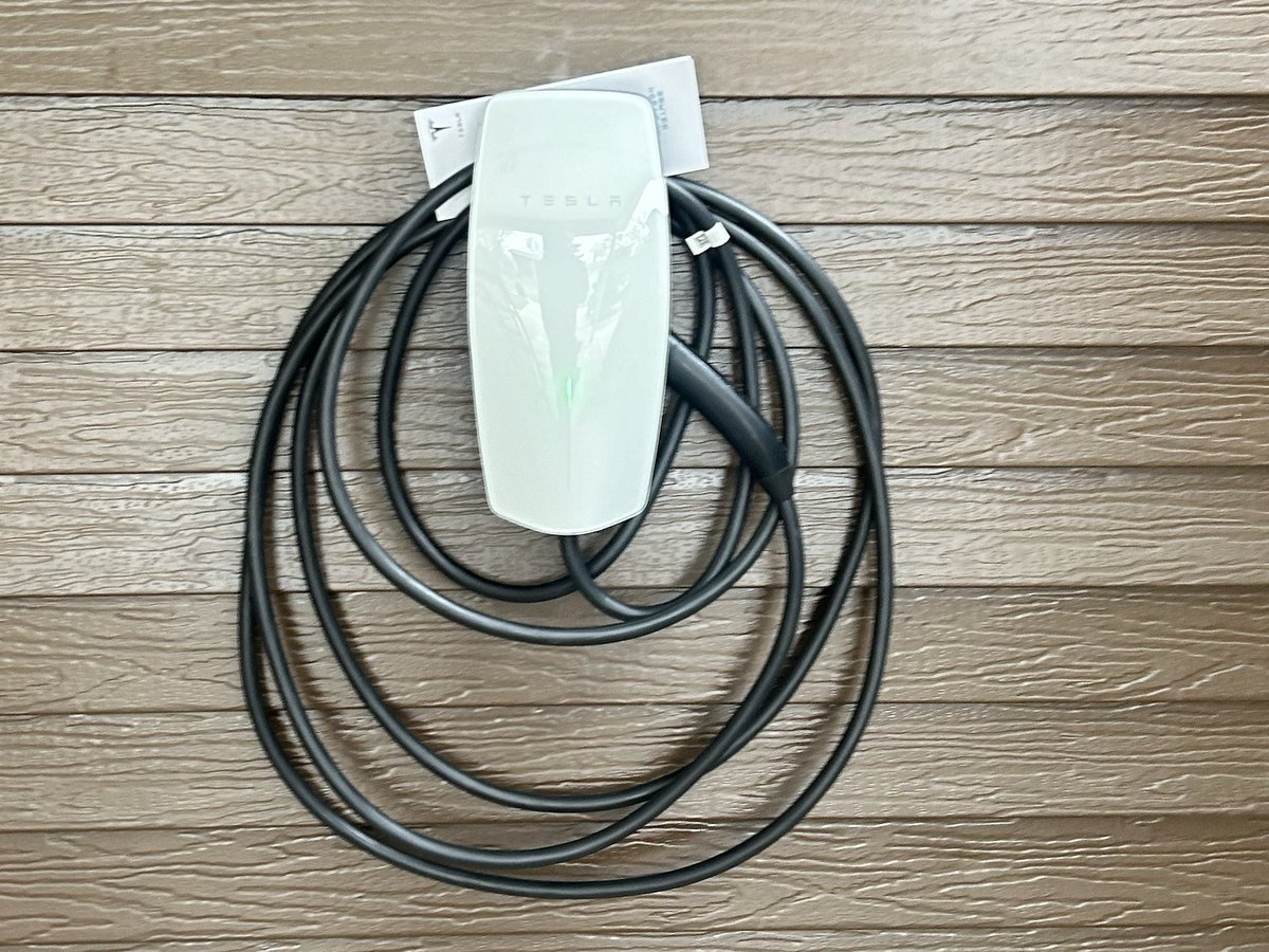White and green electric vehicle charging connector mounted on wooden wall with coiled black power cable